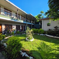 Un patio con un jardín central, un edificio con balcón y una pequeña estructura con tejado de tejas.