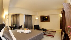Hotelkamer met een groot bed, een bureau, een stoel, een aan de muur bevestigde televisie en een bijzettafeltje met bloemen.