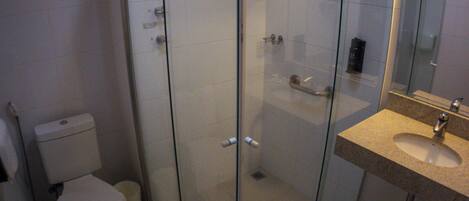 Un baño moderno con cabina de ducha de vidrio, inodoro y lavamanos con espejo.