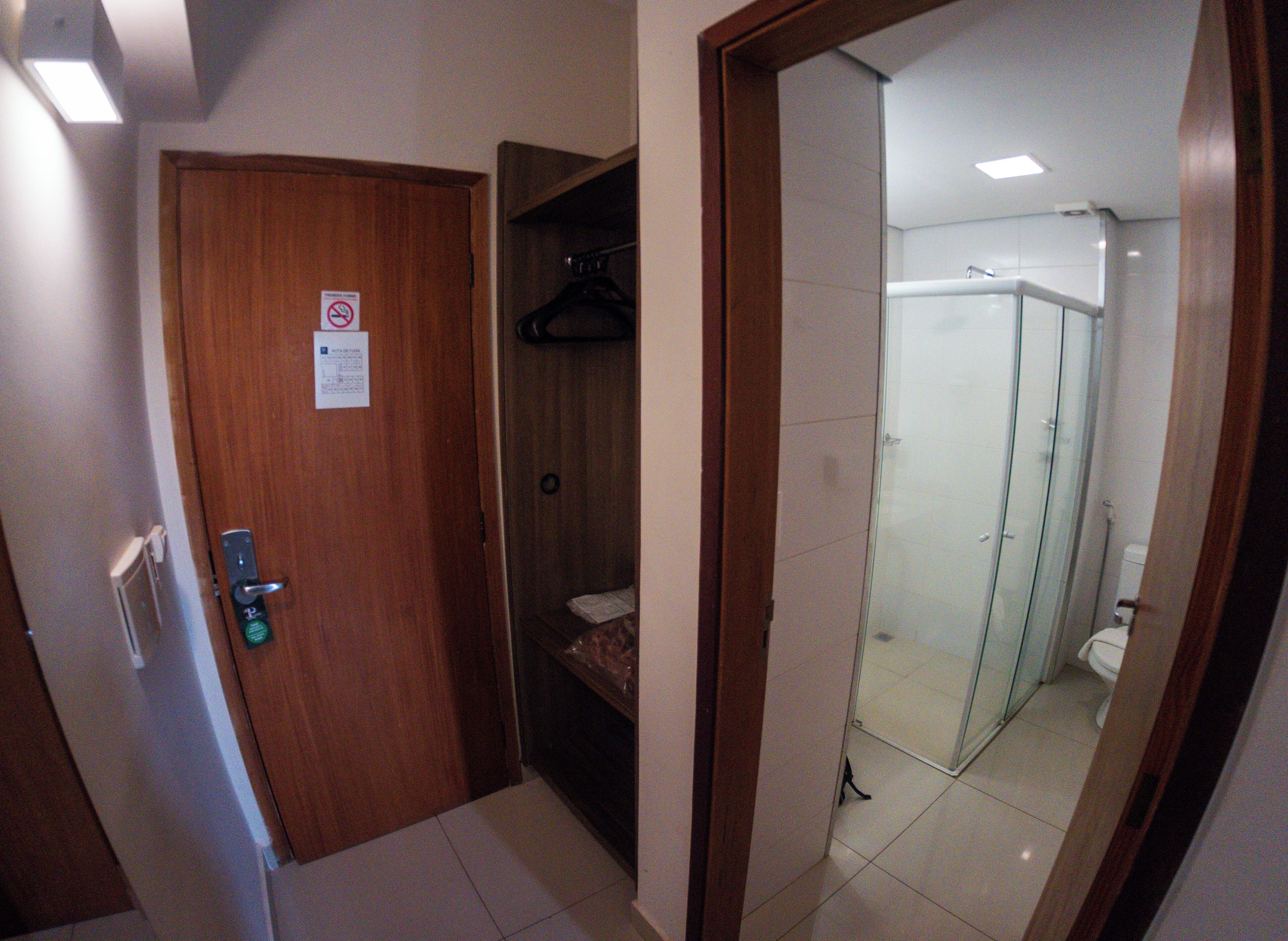 A hotel room with a wooden door, a coat rack, and a glass shower enclosure.