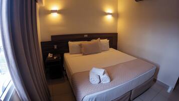 A hotel room with a large bed, two bedside lamps, a nightstand with a phone, and an air conditioning unit on the wall.