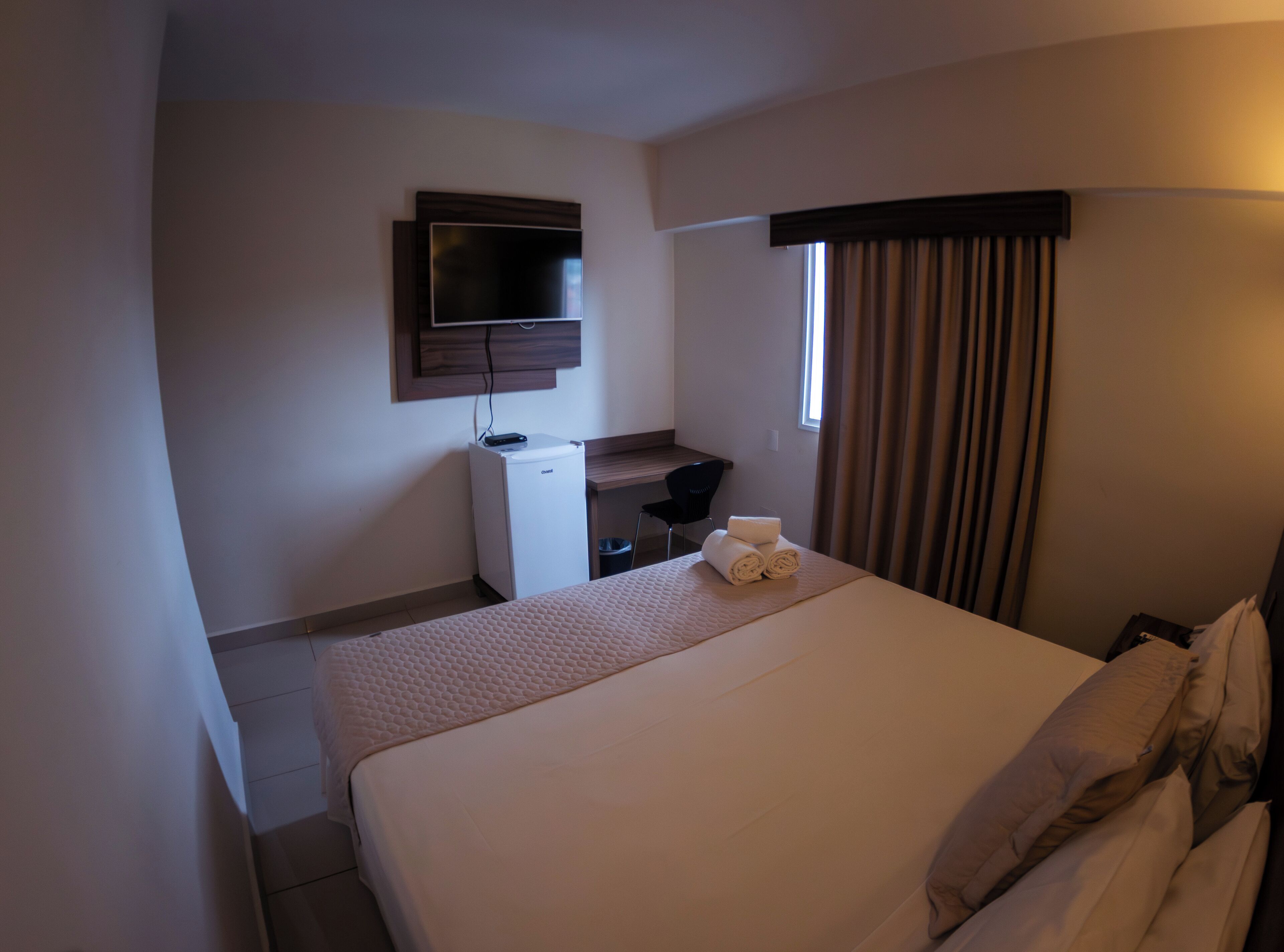 A hotel room with a bed, a desk, a television, and a window with curtains.