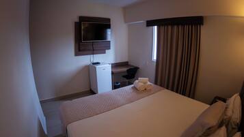 A hotel room with a bed, a desk, a television, and a window with curtains.
