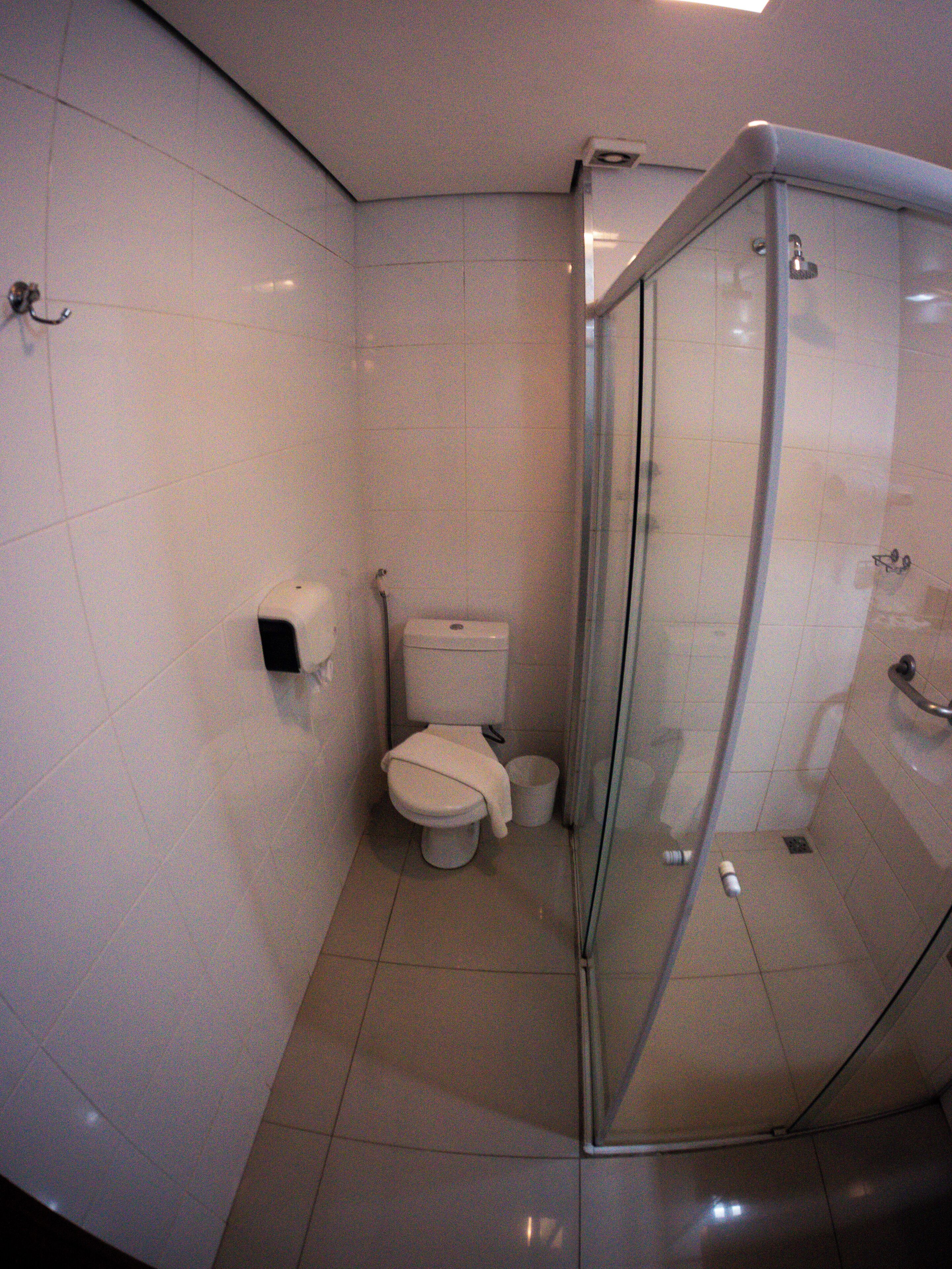 Een compacte, moderne badkamer met toilet, prullenbak en douchecabine met glazen wanden.