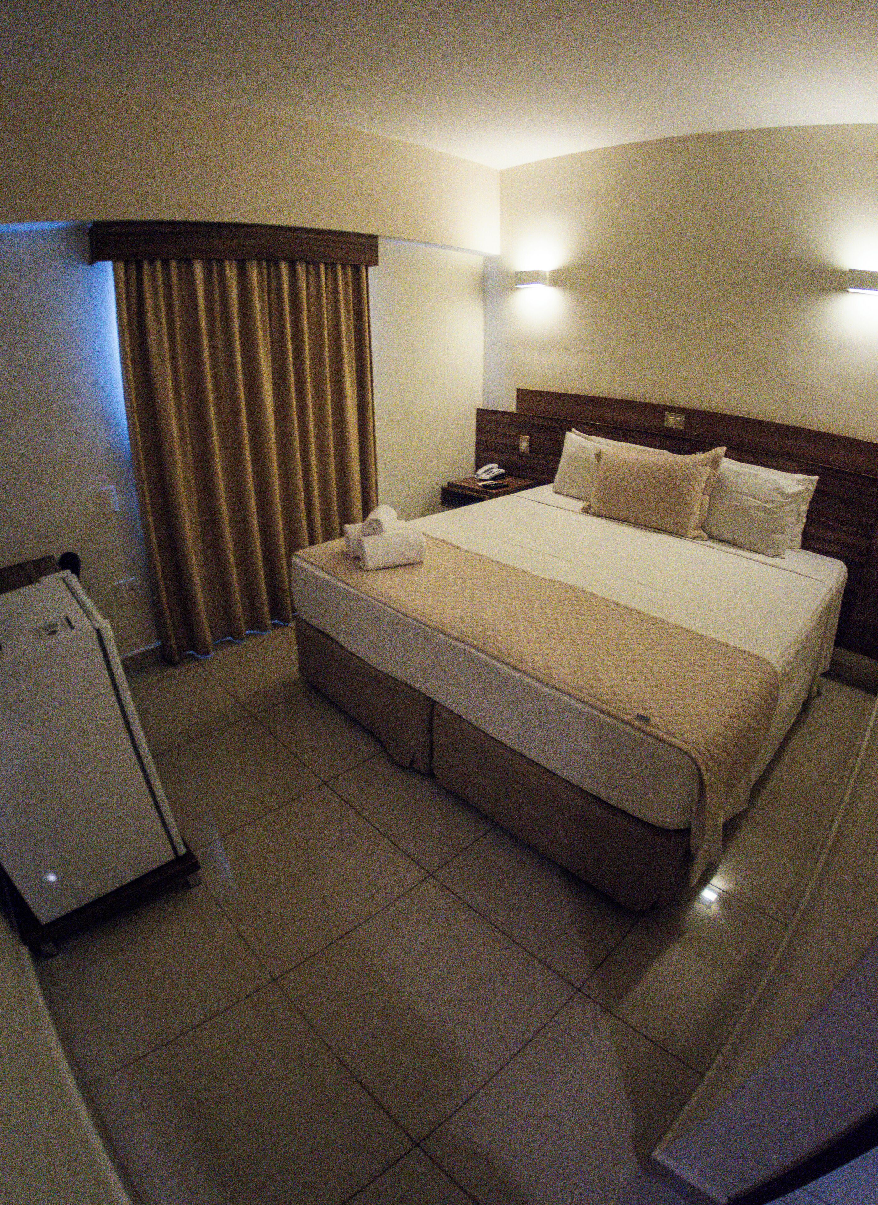 Una habitación de hotel con una cama, una mesita de noche, un teléfono y un refrigerador.