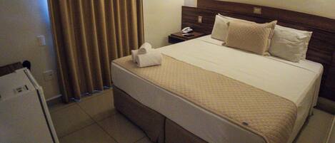 A hotel room with a bed, a nightstand, a telephone, and a refrigerator.