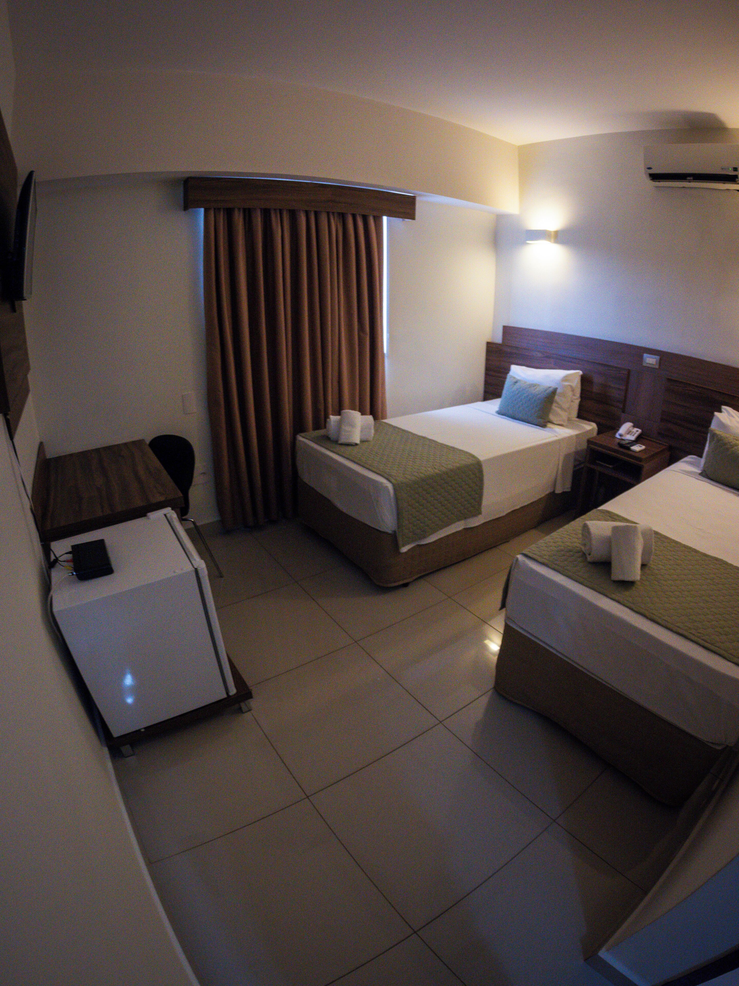 A hotel room with two beds, a desk, a chair, a small table, and an air conditioning unit.