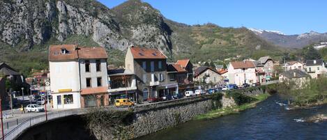 Un río con un puente de piedra, edificios con tejados rojos y montañas al fondo.