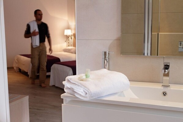 A hotel room with a large white bathtub, a mirror, and a neatly folded white towel on the edge.