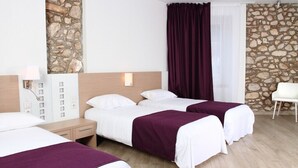 Une chambre d’hôtel avec deux lits, un mur décoratif en pierre, une chaise blanche et une table de chevet avec une lampe.