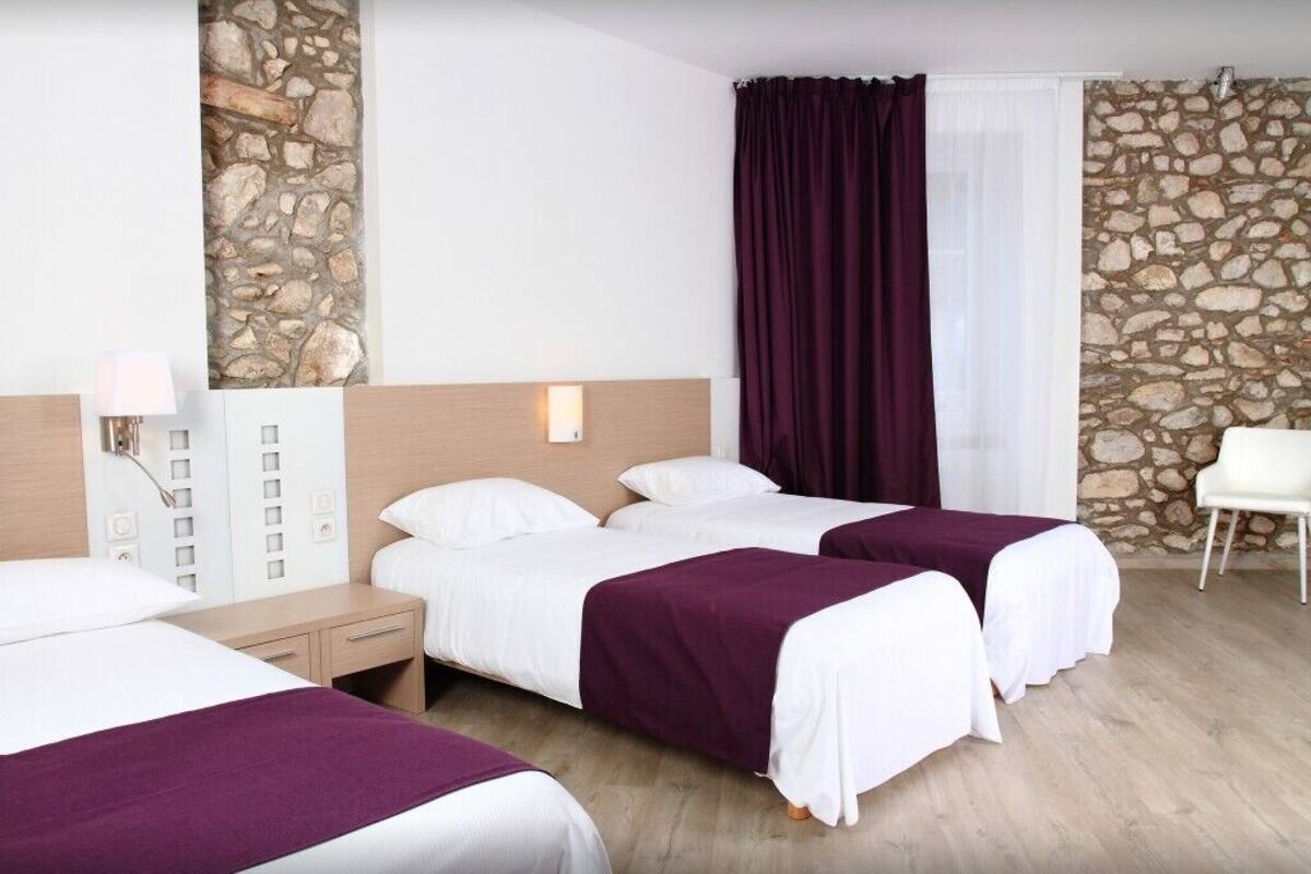 Een hotelkamer met twee bedden, een accentmuur van steen, een witte stoel en een nachtkastje met een lamp.