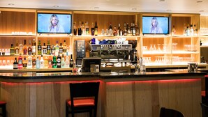 Un espace bar doté de plusieurs étagères remplies de bouteilles d’alcool, d’une machine à café et de deux téléviseurs diffusant des images d ’une personne.