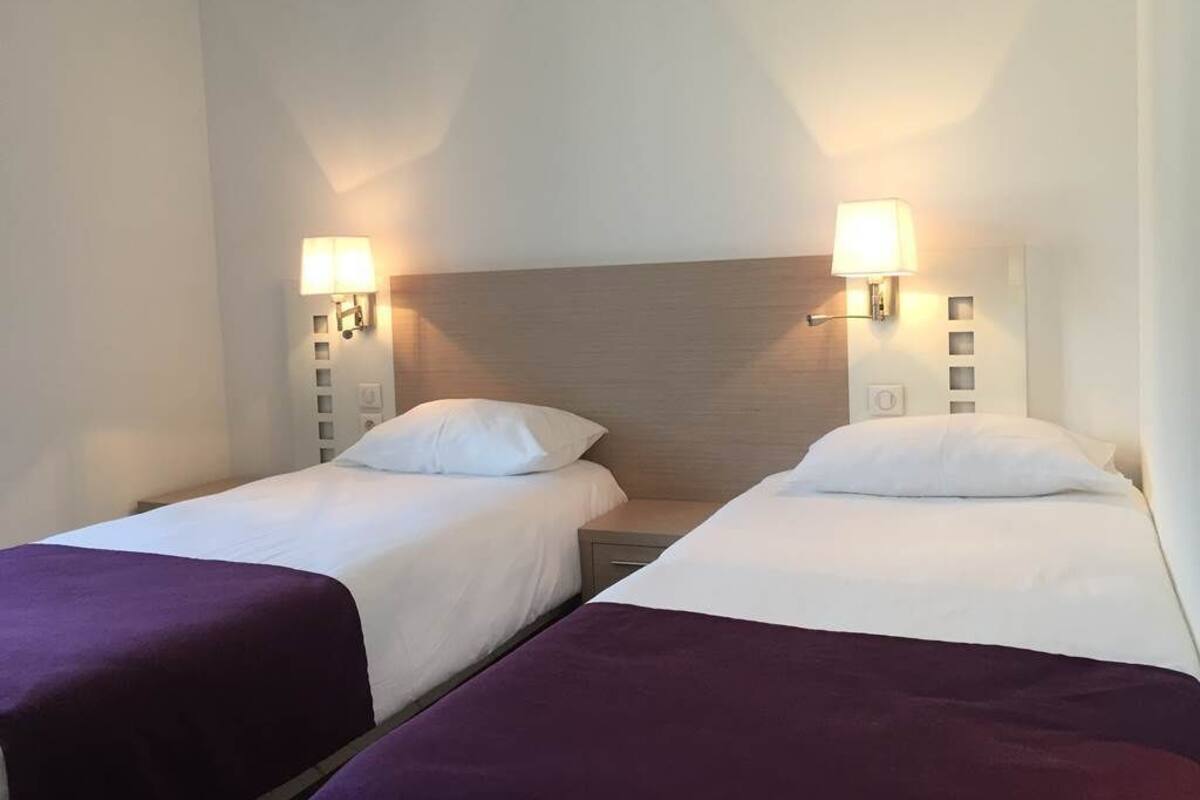Twee eenpersoonsbedden met hoofdborden, elk met een nachtkastje en een wandlamp.