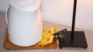 A white electric kettle on a wooden coaster, a black stand, and two packets of Lipton tea on a tray.