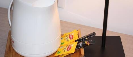 A white electric kettle on a wooden coaster, a black stand, and two packets of Lipton tea on a tray.