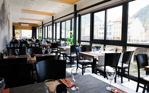 A restaurant with tables set for dining, large windows offering a view of buildings and mountains.