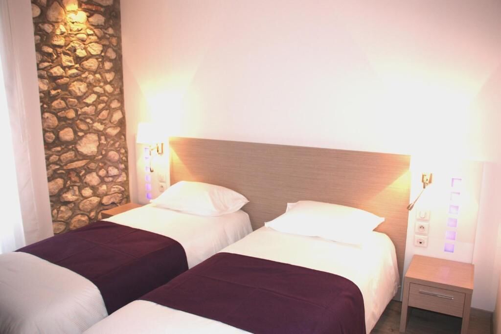 A hotel room with two beds, a stone wall, and a wooden headboard.