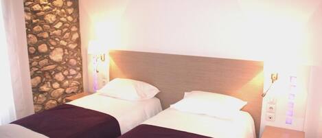 A hotel room with two beds, a stone wall, and a wooden headboard.