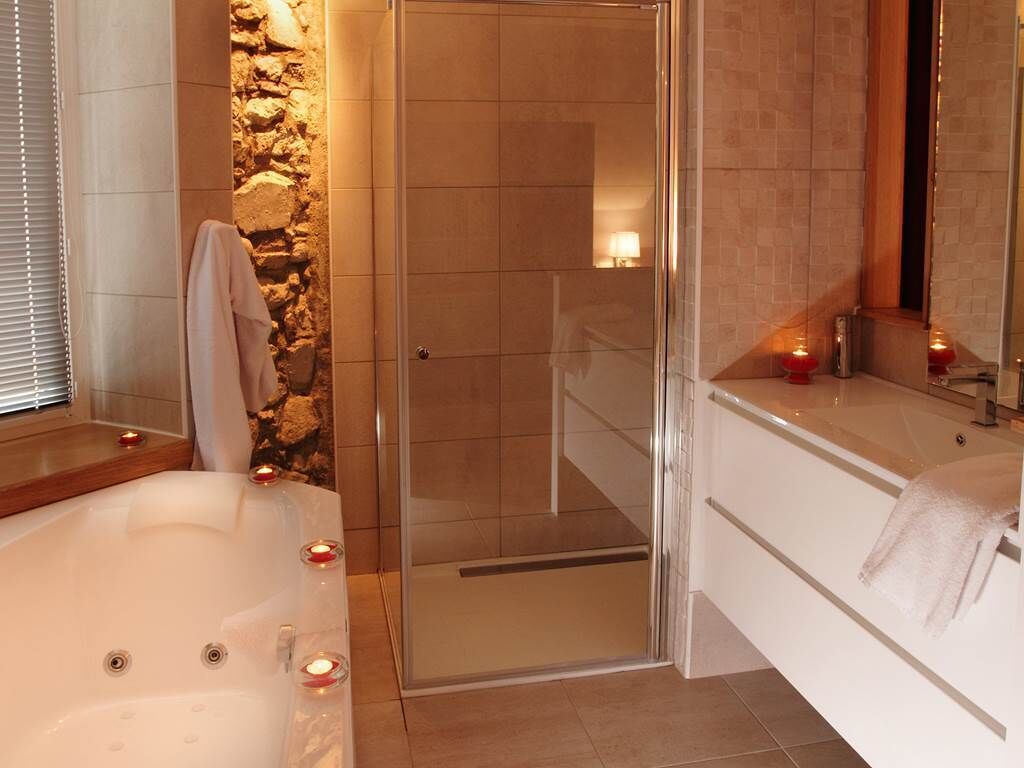 A bathroom with a bathtub, a glass shower enclosure, a vanity with a mirror, and candles on the counter.