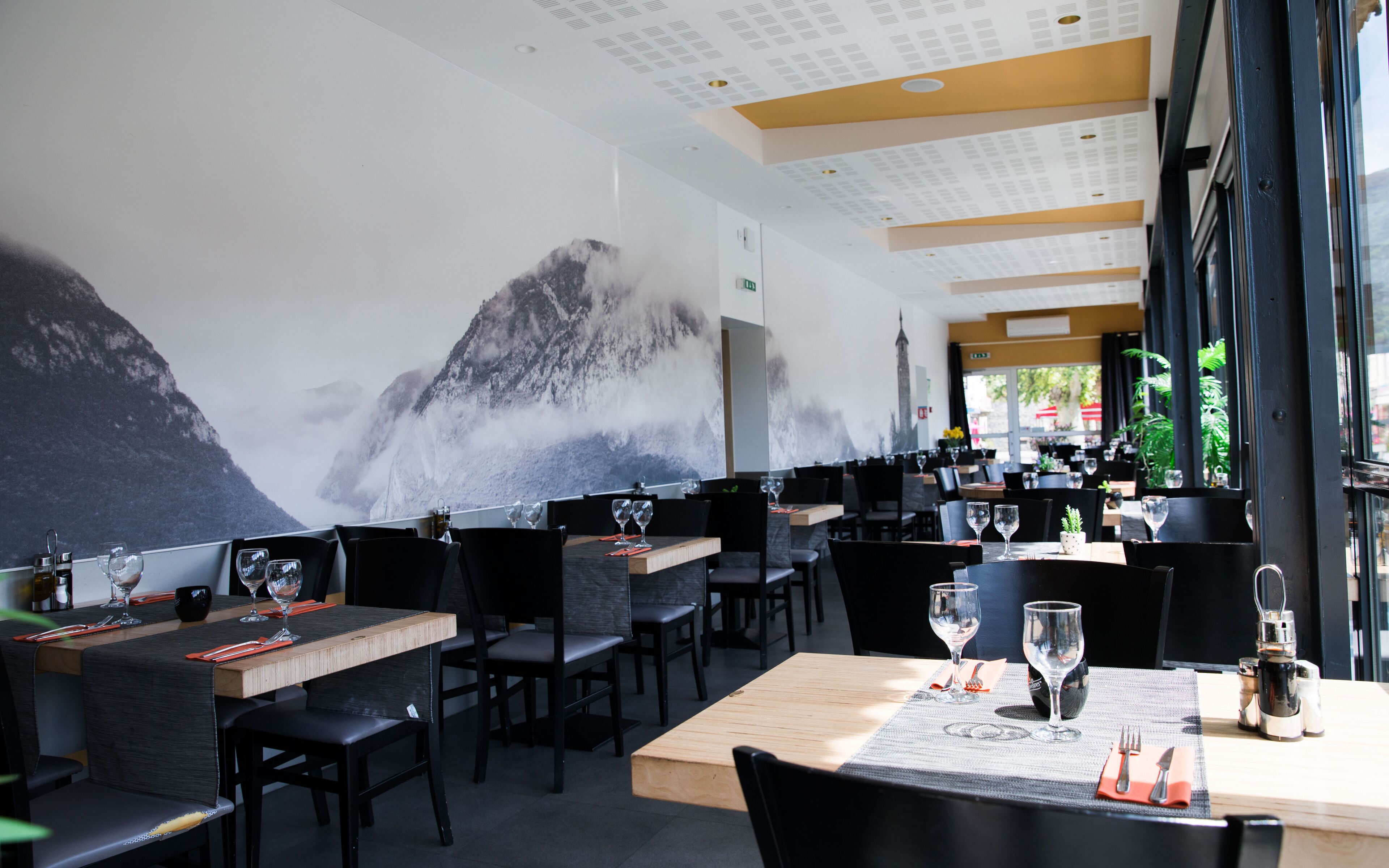A restaurant with tables set for dining, chairs, and a large mural of a mountain on the wall.
