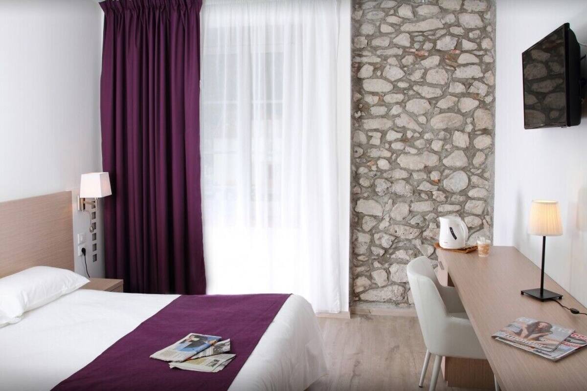 Een hotelkamer met een bed, een bureau, een stoel, een stenen muur en een raam met gordijnen.