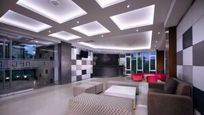 A modern hotel lobby with a glass wall, a reception desk, and a seating area with sofas and ottomans. - Hotel Neo Denpasar by ASTON (Denpasar)
