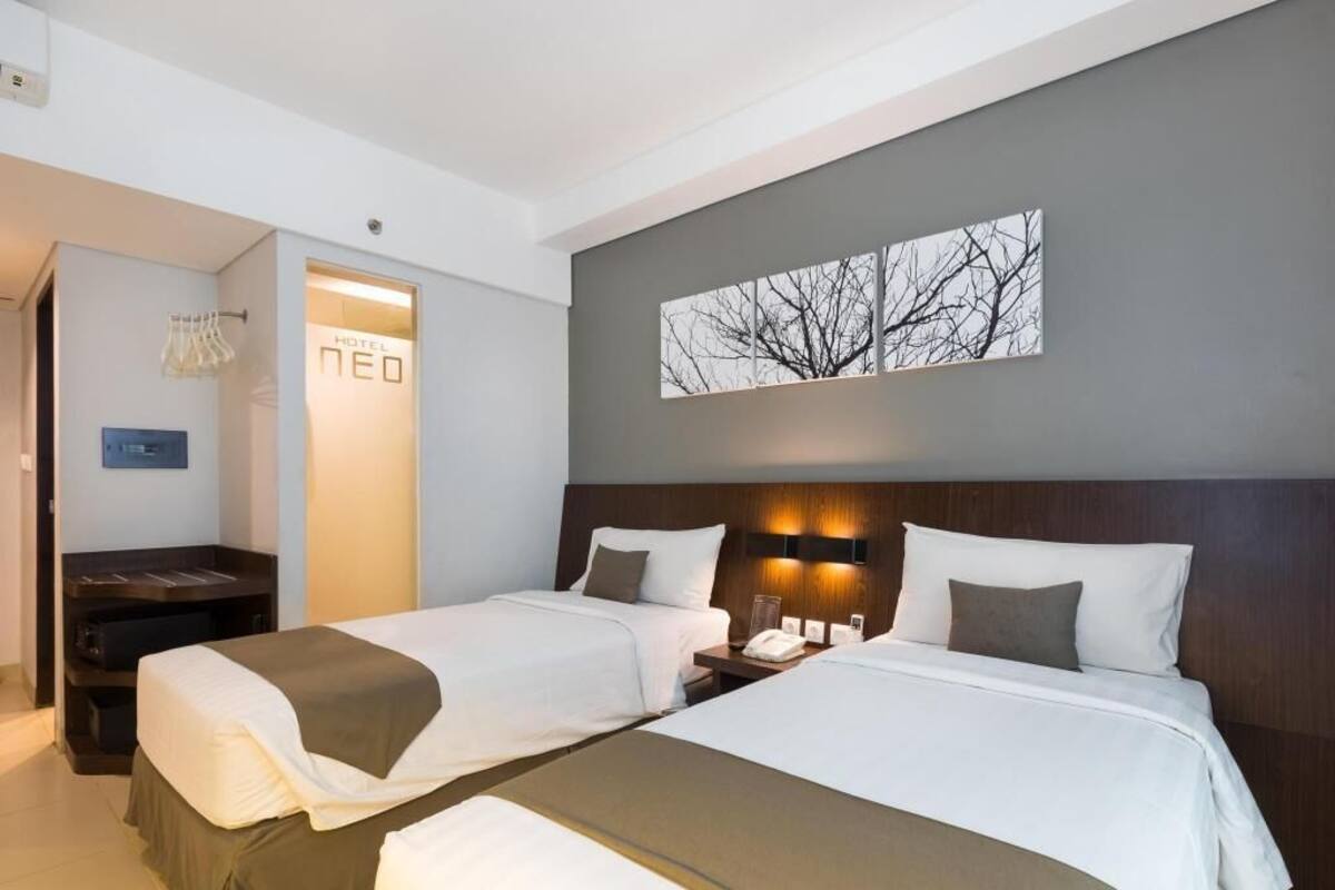 A hotel room with two beds, a nightstand, a desk, and a wall-mounted artwork.
