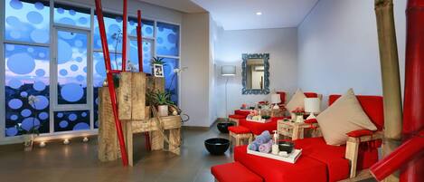 Un spa moderno con un sofá rojo, muebles de madera y un amplio ventanal con vistas al cielo.