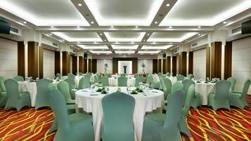 Une salle de banquet avec des tables rondes, des chaises vertes et un tapis à motifs.