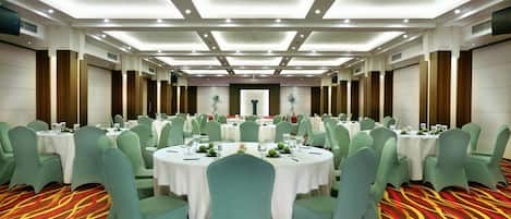 A banquet hall with round tables, green chairs, and a patterned carpet.