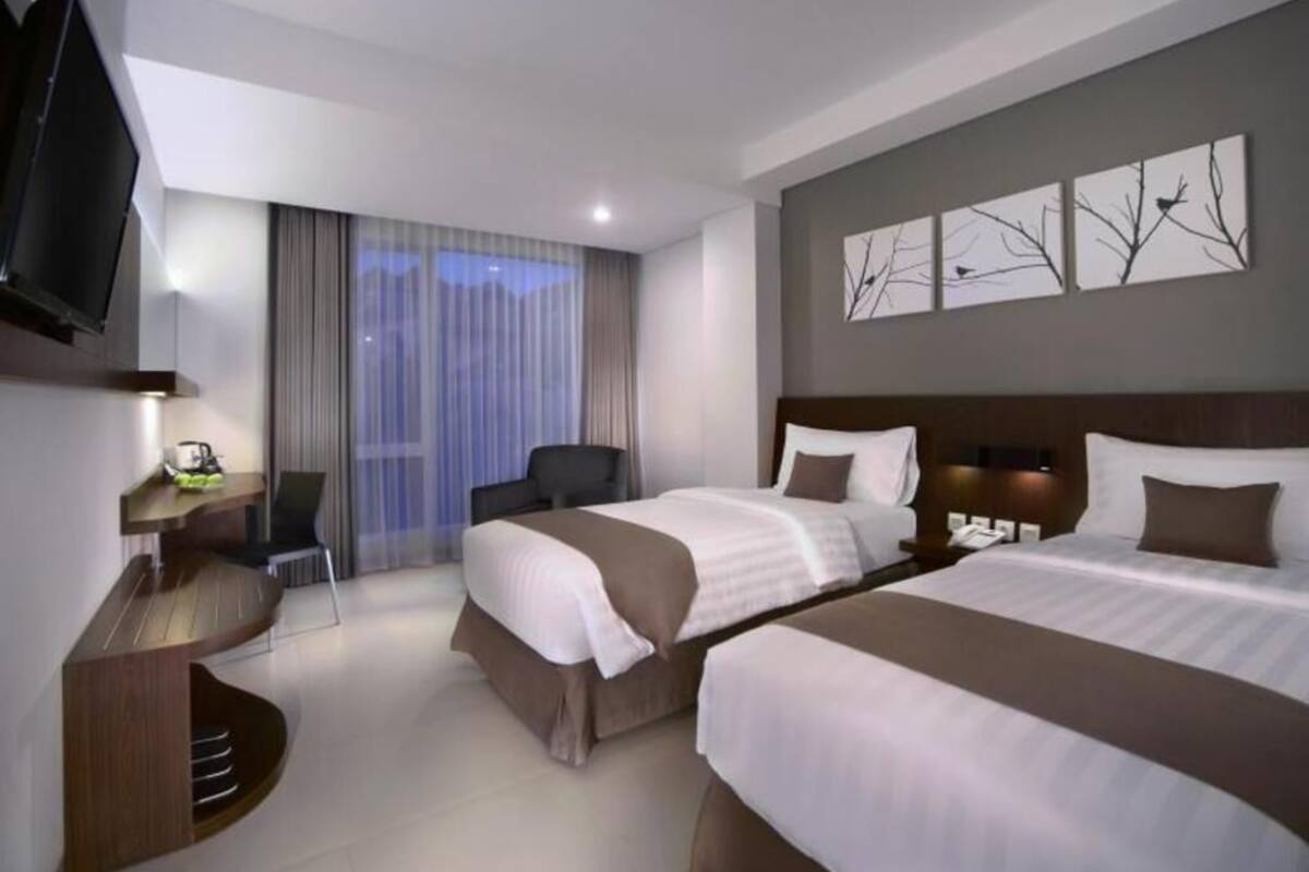 A hotel room with two beds, a TV, a desk, and a chair.