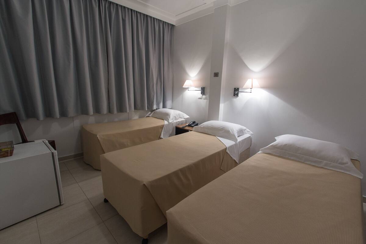 Ett hotellrum med tre separata sängar, ett skrivbord och två väggmonterade lampor.