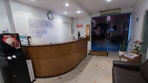 A reception area with a wooden reception desk, a clock on the wall, and a digital coffee machine. - Oyo Uniclass Hotel Centro SP (Sao Paulo)