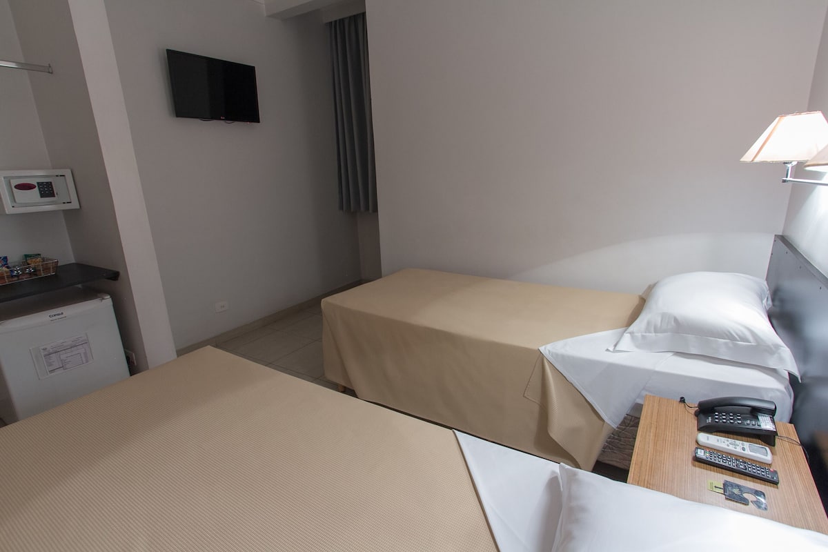 Ett hotellrum med två sängar, ett skrivbord med en lampa, en TV och en minibar.