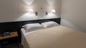 A hotel room with a bed, two bedside lamps, a nightstand with a phone and remote control, and a sign on the wall. - Oyo Uniclass Hotel Centro SP (Sao Paulo)