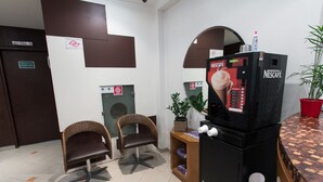A Nescafé coffee machine, two wicker chairs, a small wooden table, and a potted plant in a room with tiled flooring and brown walls. - Oyo Uniclass Hotel Centro SP (Sao Paulo)