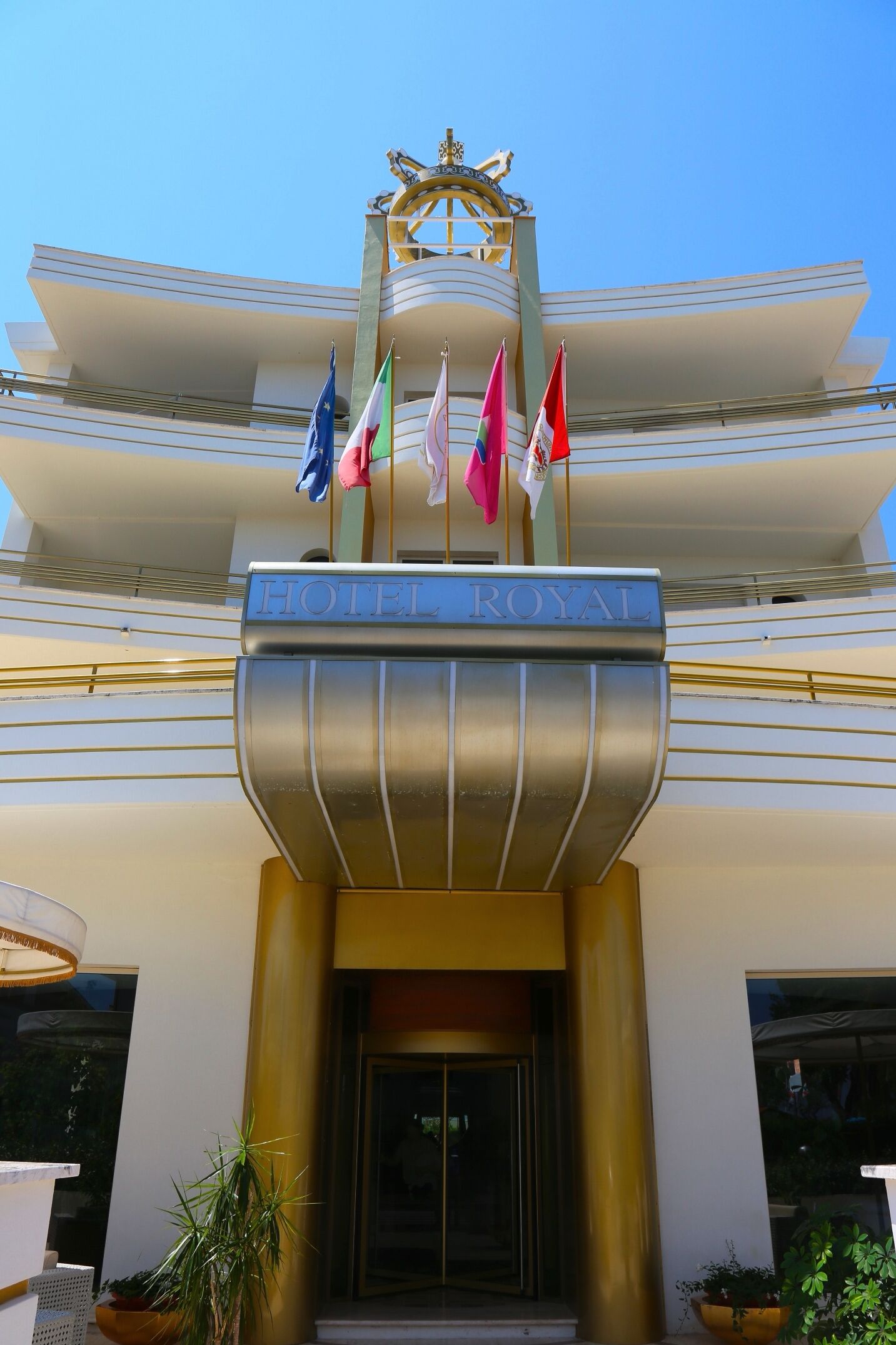 The entrance of the HOTEL ROYAL with a prominent sign, multiple flags, and a decorative emblem above the entrance.