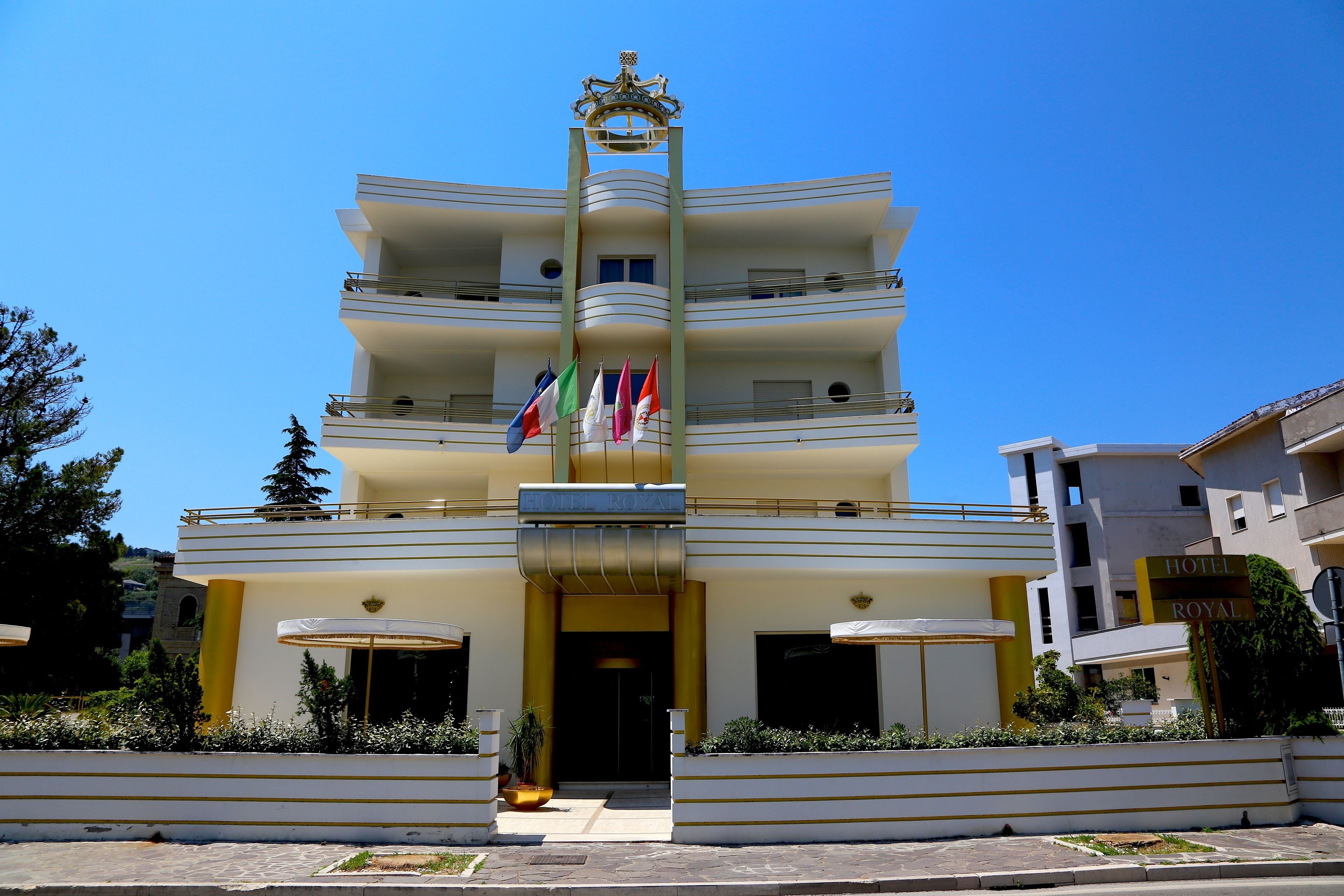 A multi-story hotel with balconies, a central entrance, and flags.