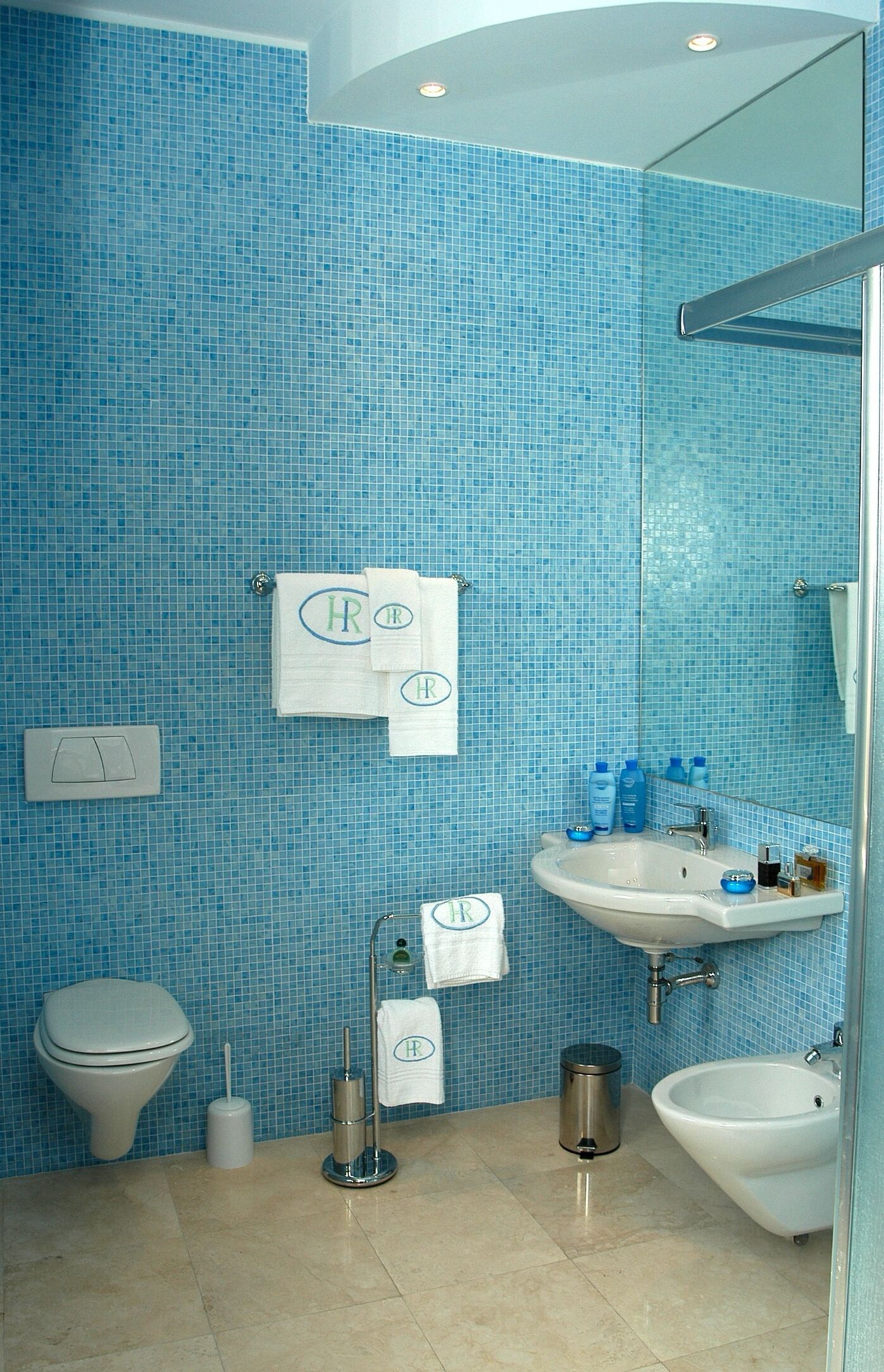 Une salle de bain avec des carreaux de mosaïque bleus, des toilettes, un bidet, un lavabo et un miroir.