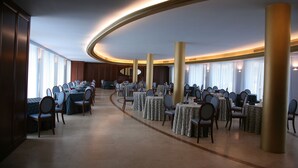 A spacious banquet hall with multiple round tables and chairs, large columns, and a curved ceiling. - Hotel Royal (Vasto)