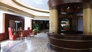 A lobby with a reception desk, red chairs, a large mirror, and a patterned floor. - Hotel Royal (Vasto)
