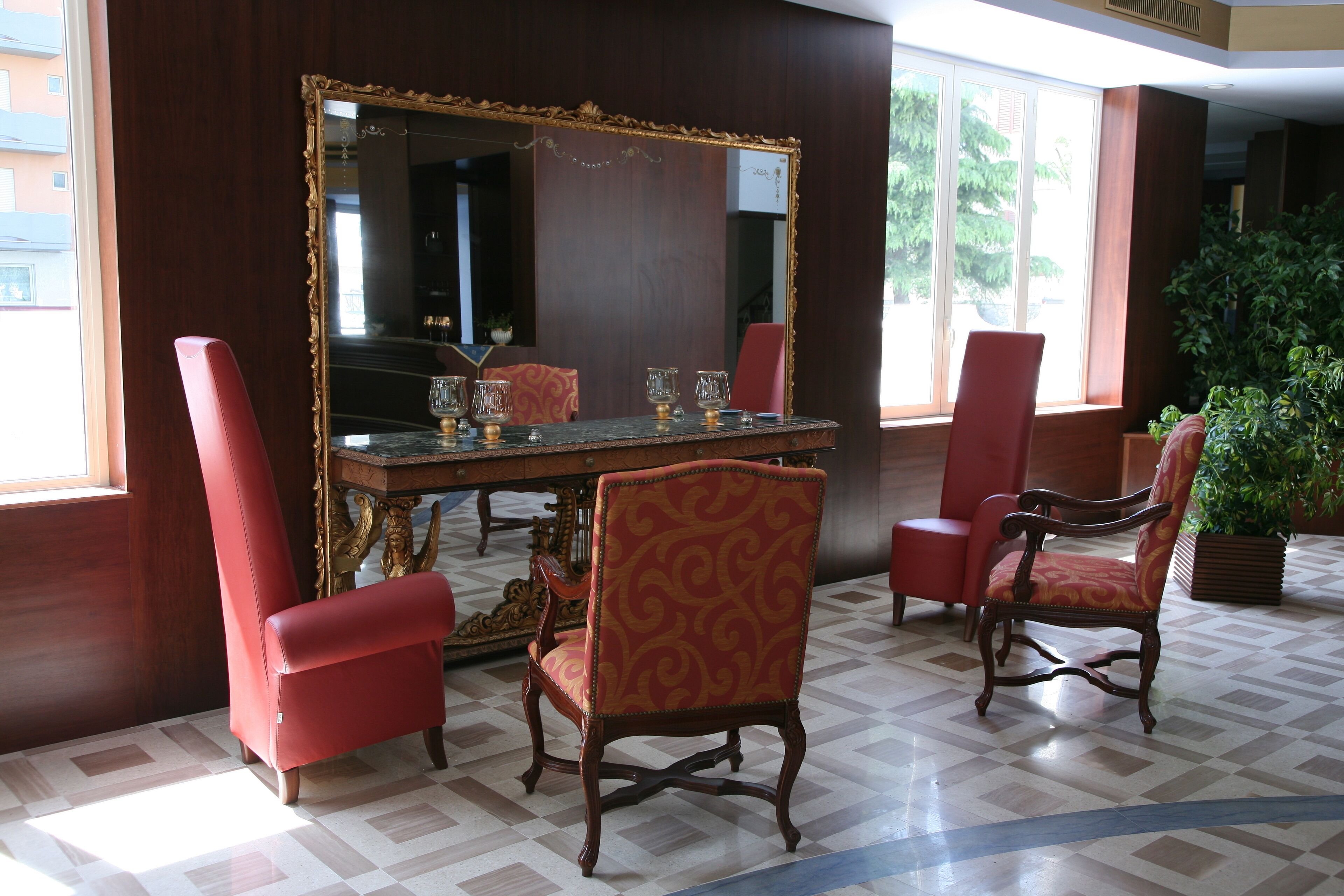 Een eethoek met een grote spiegel, een gedekte tafel met glazen en rode fauteuils.