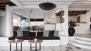 Un interior moderno con un sofá blanco y negro, dos mesas redondas de madera y una gran planta en maceta.