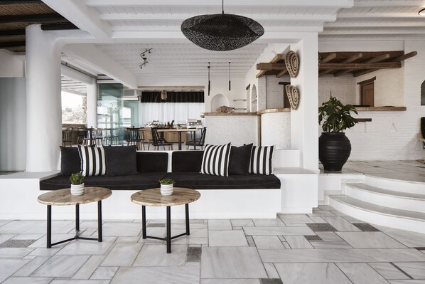 Un intérieur moderne avec un canapé noir et blanc, deux petites tables rondes en bois et une grande plante en pot.