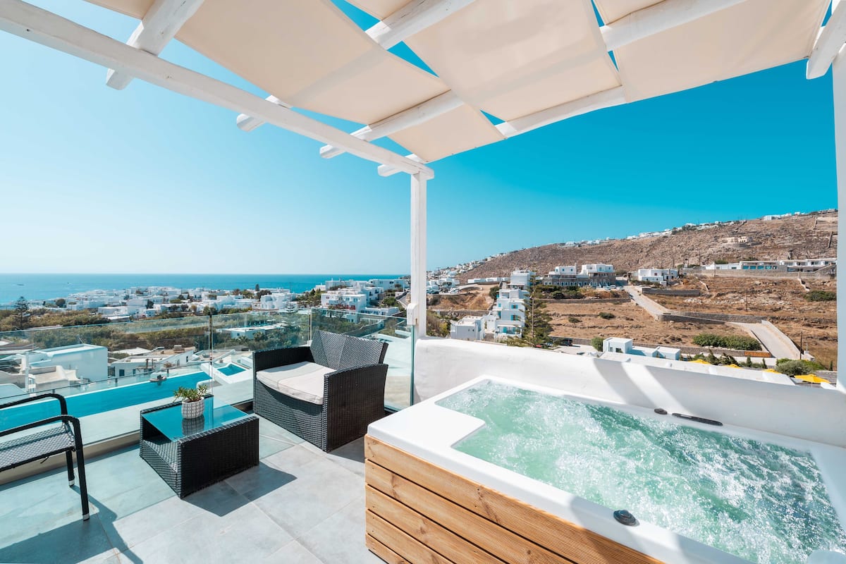 Une terrasse sur le toit avec un jacuzzi, des sièges extérieurs et une piscine, offrant une vue sur une ville côtière.