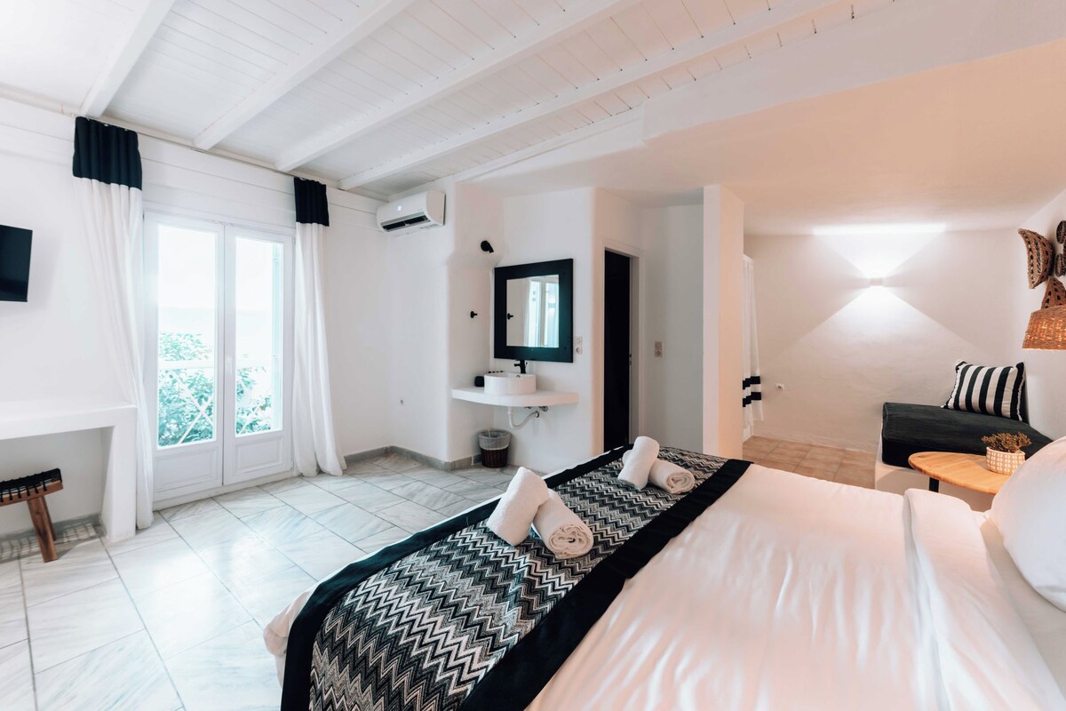Habitación de hotel con cama, escritorio, silla, una mesita y ventana con cortinas.