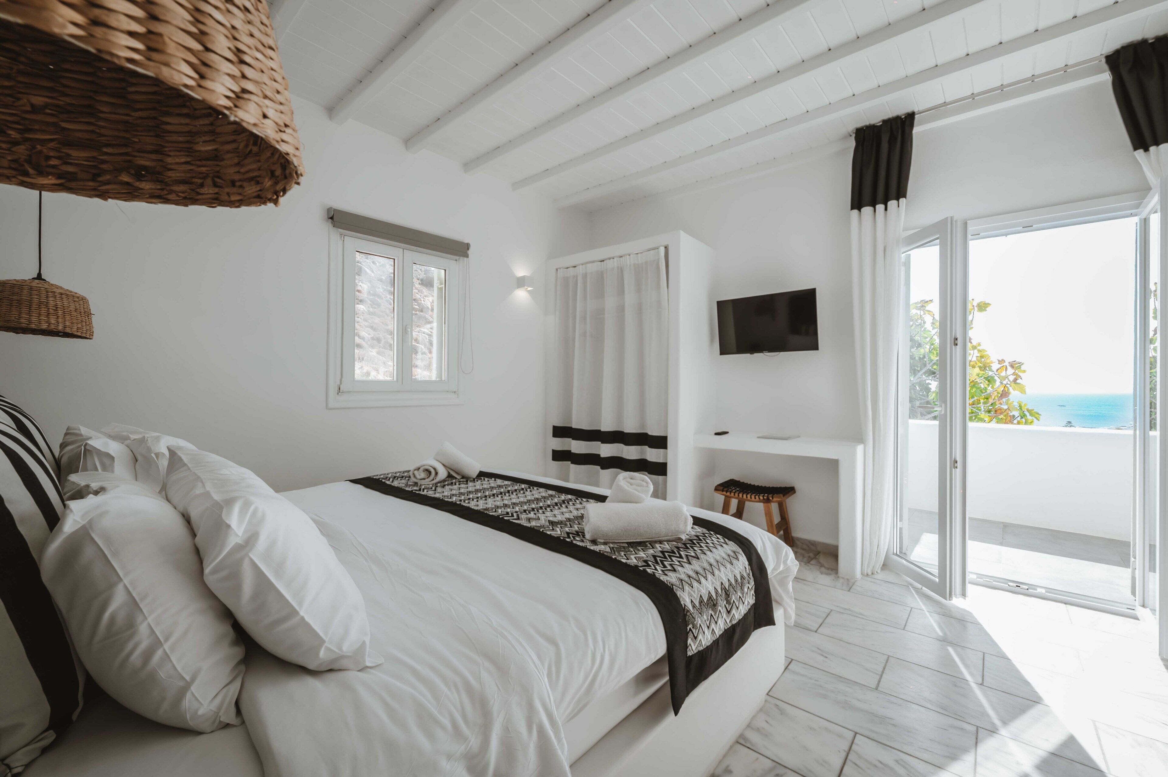 A hotel room with a bed, a TV, a desk, and a view of the sea.