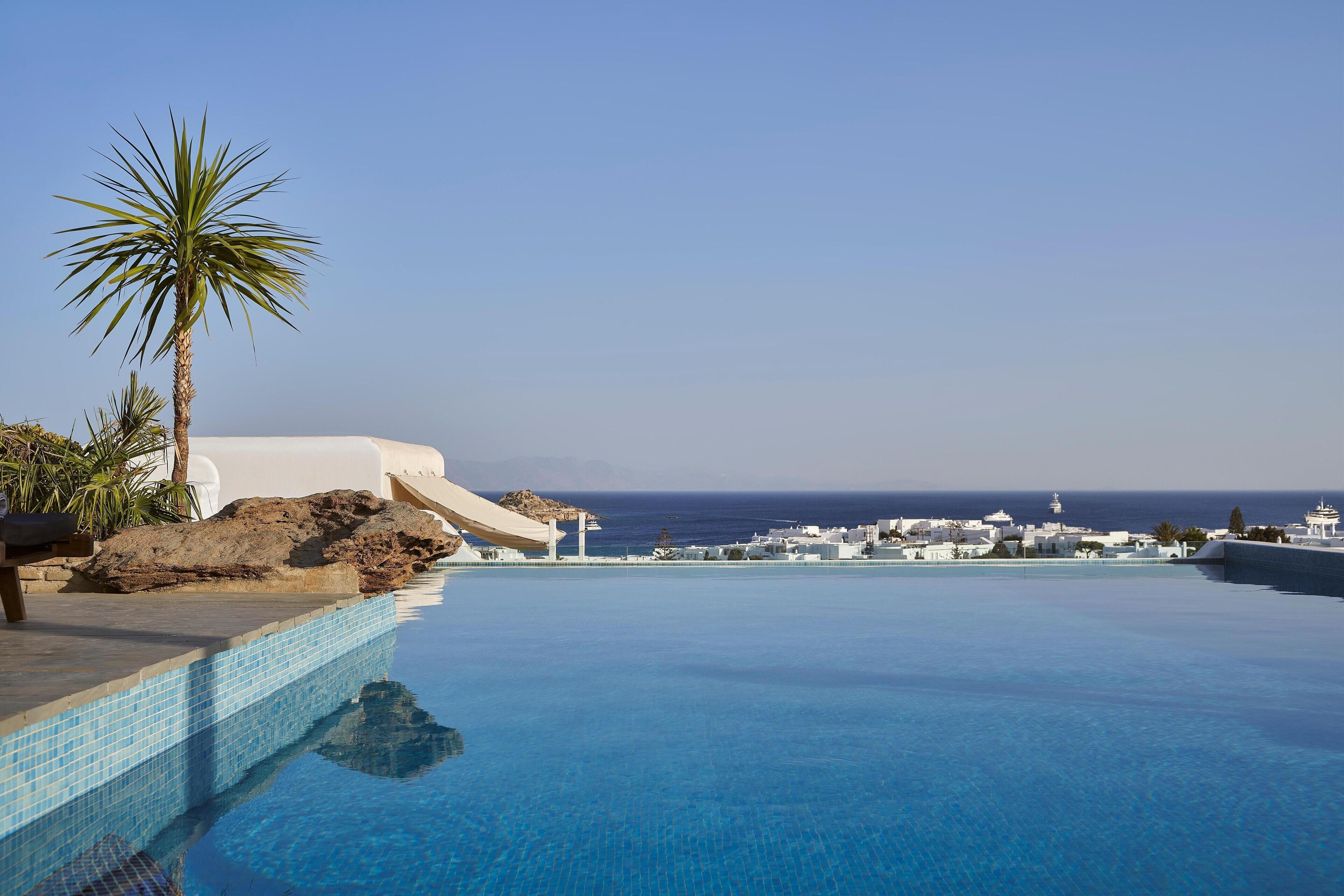 A clear blue pool with a view of the sea and white buildings in the background.
