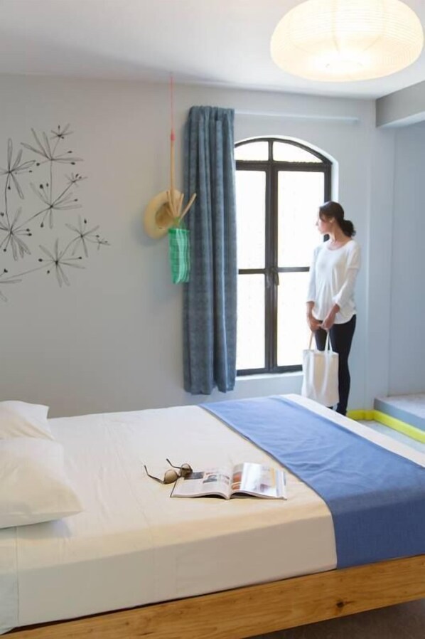Une chambre à coucher avec un lit, une fenêtre avec des rideaux, un tableau décoratif au mur et un chapeau suspendu.