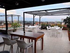 An outdoor patio with tables and chairs, a view of the cityscape, and potted plants.